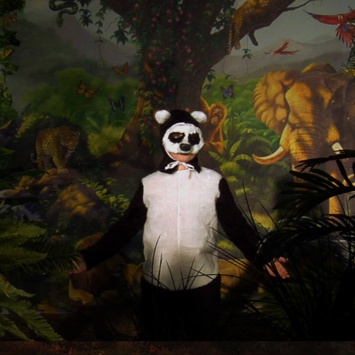 A person dressed as a panda standing in front of a painted jungle background. 